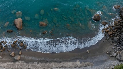 Aerial view of turquoise coastal water meeting a rocky beach with numerous boulders and white ocean waves.