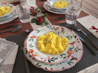 Table setting with bright tableware, berries, and twigs. Saffron risotto on plate. Traditional Italian food. Aesthetics and lifestyle. Interior design. 