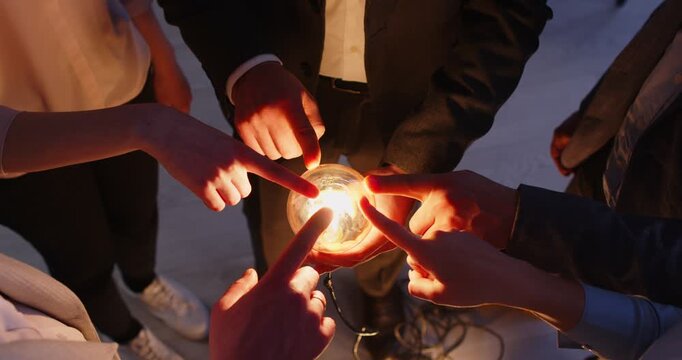 Business people group putting fingers on illuminated lightbulb standing in a circle sharing creative energy and innovative ideas. Teamwork, cooperation and success concept. 4l video.