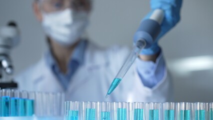 Woman scientist researcher using a micropipette to fill up test tubes with a blue liquid in laboratory setting, closeup view. Medicine and science concept