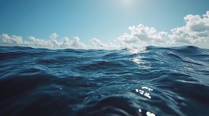 A tranquil ocean view with gentle waves under a bright sky filled with fluffy clouds.
