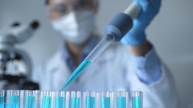 Close up of a female scientist researcher hand using a micropipette to fill up test tubes with a blue liquid in laboratory. Medicine and science