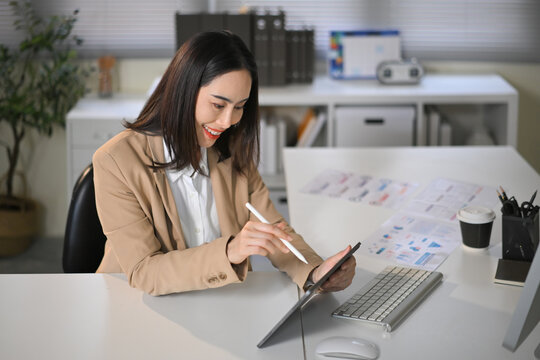 Smiling businesswoman using tablet and stylus pen in modern office, reviewing data and working on digital project with confidence and focus