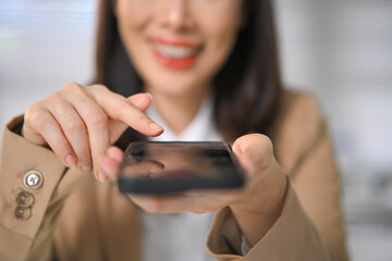 Close-up of businesswoman using smartphone, tapping screen with focus and smile