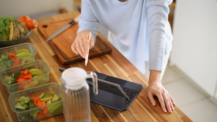 Top view woman using tablet to follow online recipe while preparing healthy food in kitchen