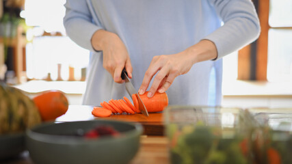 Closeup of young female hands chopping fresh orange carrot on board while in modern kitchen