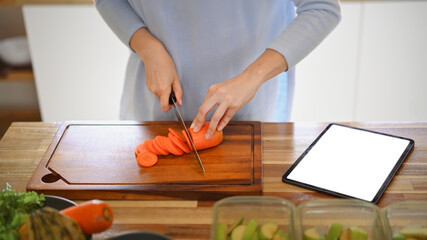 Closeup of young female hands chopping fresh orange carrot on board while in modern kitchen