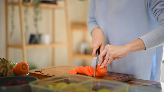 Closeup of young female hands chopping fresh orange carrot on board while in modern kitchen - Powered by Adobe