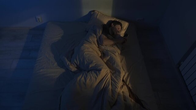 Sleepless man in bed using smartphone at night, insomnia concept