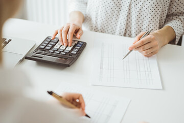 Accountant using a calculator and laptop computer for counting taxes with a client or a colleague at white desk in office. Teamwork in business audit and finance