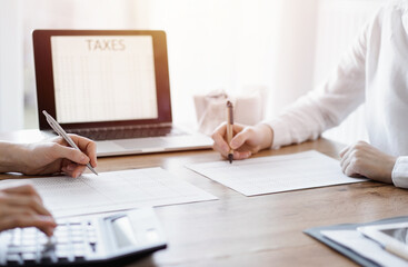 Two accountants using a laptop computer and calculator while counting taxes at wooden desk in office. Teamwork in business audit and finance