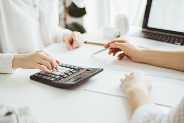 Accountant using a calculator and laptop computer for counting taxes with a client or a colleague at white desk in office. Teamwork in business audit and finance