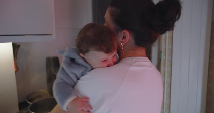 Mother cradling baby on shoulder in kitchen surrounded by pots and pans, concept of parenthood, domestic life, and unconditional love