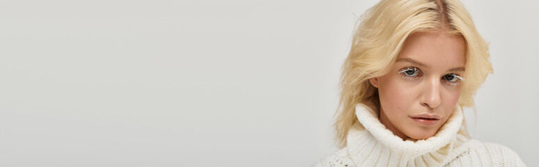 Cozy blonde beauty in a knitted sweater posing gracefully in a serene studio space