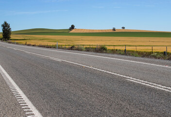 Rural highway and golden farmland under clear blue sky