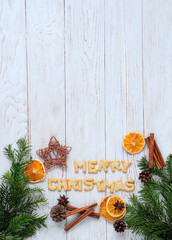 Christmas holiday background. Dry orange slices, cinnamon sticks, fir branches and Merry Christmas text made of cookies on white wooden table. Advent time, winter festive season. flat lay. copy space