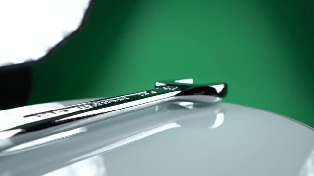 Close-up of a shiny metal wrench on a reflective surface with a green background, showcasing precision tools.
