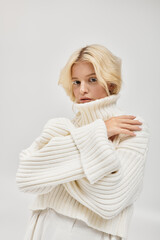 Young blonde woman in cozy knitted sweater posing elegantly in a bright studio