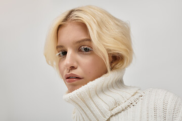 Blonde beauty in cozy sweater showcases winter fashion in tranquil studio setting