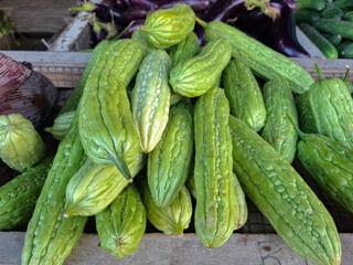 Pile of fresh green bitter gourds (Momordica charantia) on a wooden stall at a market. Tropical vegetable