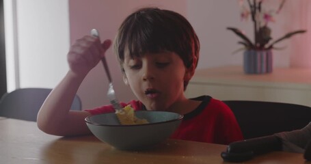Older child eating meal while baby beside him waves spoon playfully, concept of family routine, sibling dynamic, and early imitation during mealtime - Powered by Adobe