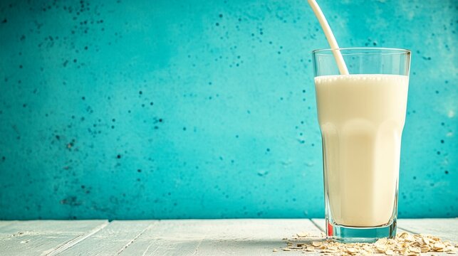 Refreshing glass of creamy milk with a straw, set against a vibrant turquoise background, resting on a rustic wooden surface with scattered oats
