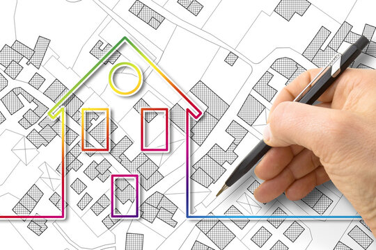 Architect drawing a residential building over an imaginary cadastral map of territory with buildings, fields and roads