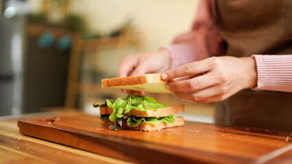 woman prepares a sandwich at home, layering ham and fresh vegetables in a warm, natural light kitchen