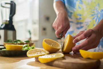 Young boy slicing fresh lemon on wooden cutting board in kitchen, hands holding knife and lemon, preparing ingredients for healthy meal or beverage