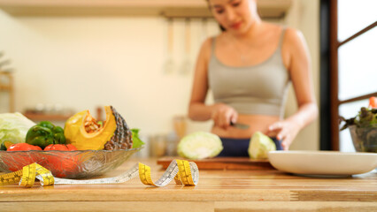 slim woman cooking salad with fresh vegetables near measuring tape on kitchen table