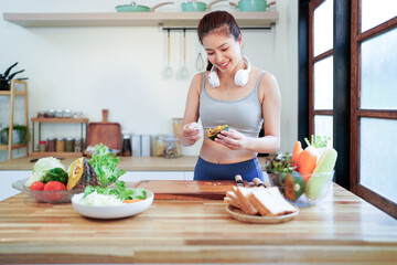 A good looking woman wearing a sports suit is making a salad in the kitchen at home