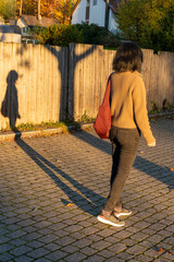 Asian woman is walking into an autumn evening with low sun, creating long shadows, and warm colors.