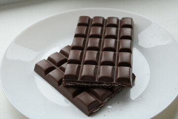 Broken dark chocolate bar pieces arranged on white plate showing interior texture and segmented chocolate structure. dark chocolate with nuts