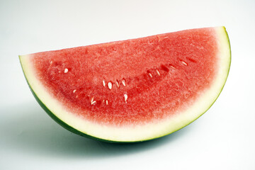 Close-up of a refreshing wedge of ripe red watermelon showing seeds and green rind, isolated on a clean white background, perfect for summer themes.
