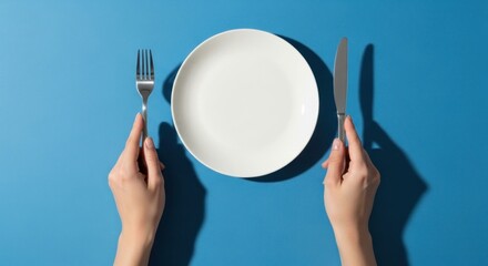 Hands flanking an empty plate with a fork and knife on a blue surface