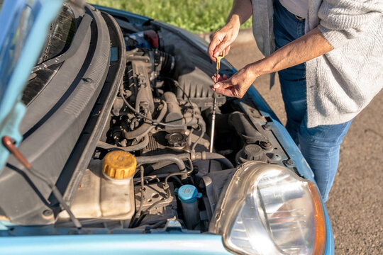 Close-up of woman checking car oil dipstick on roadside during vehicle breakdown