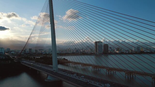 Modern cable-stayed bridge over Han River in Da Nang, Contemporary urban span connecting city skyline across Vietnamese waterway, aerial drone view 4k