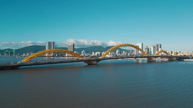 Golden Dragon Bridge over Han River in Da Nang at sunset, Iconic Vietnamese landmark over urban waterway with city skyline, aerial drone view 4k
