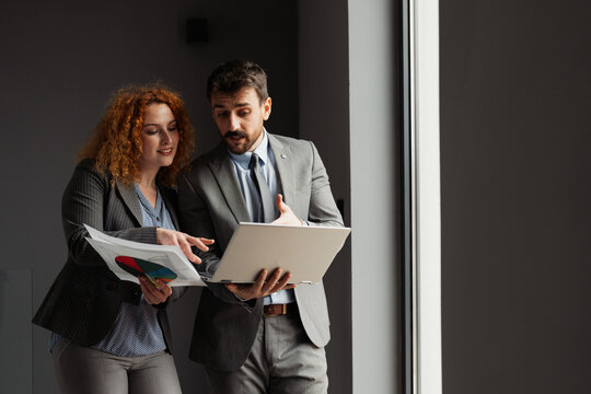 Businessman and businesswoman working together in a modern office, analyzing business data on a laptop.

