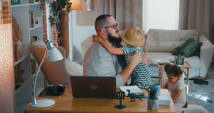 Working father comforts his crying child after a minor injury during play, showing emotional support and the importance of being there while working online from home.