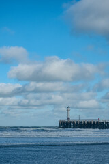 vertical shot of coastal lighthouse scene, bright beacon stands amidst rolling sea under clear skies