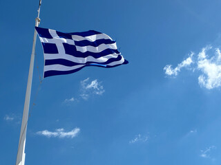 Greek flag waving proudly on a white flagpole against clear blue skies — symbol of Greece and Mediterranean identity.