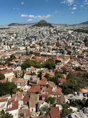 Aerial view of Athens with red rooftops leading to distant mountains under a bright blue sky.