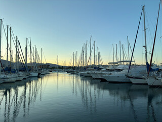 Boats and masts create striking silhouettes against calm blue waters and a glowing sunset horizon.