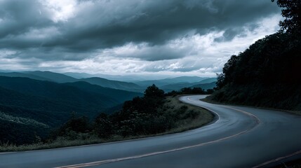 Winding mountain roadway curves through dark, layered hills beneath heavy overcast sky