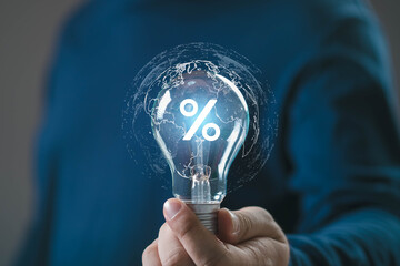 Hand holding a glowing light bulb with a percent symbol and digital world map, representing finance, interest rate, global economy, investment, and innovative financial ideas in technology.