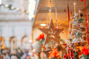 Wooden star ornament hanging with blurred festive winter market background and bokeh lights.