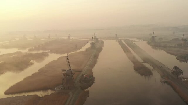 Aerial view of historic Kinderdijk windmills standing tall amidst the waterways, with a golden hue from the soft light, Kinderdijk, South Holland, Netherlands.