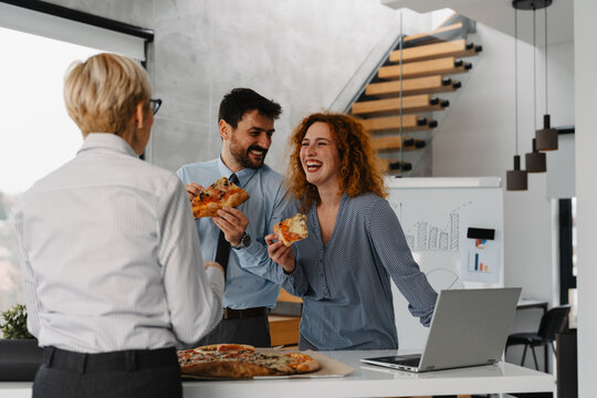 Three business people eating pizza during a lunch break in the office. Colleagues enjoying casual teamwork and relaxation time