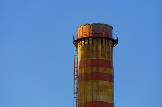 Close up detail of a weathered concrete chimney surface with faded red and white stripes showing the texture of old industrial structures and environmental wear at a thermal energy generation facility - Powered by Adobe